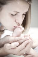 Young mother kissing foot of ...
