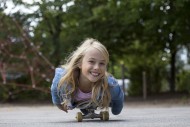 Girl (10) lies on skateboard,...